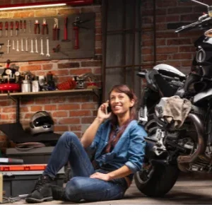 In einer Hobby Motorrad-Werkstatt sitzt einer Frau die vor ihrem Motorrad telefoniert
