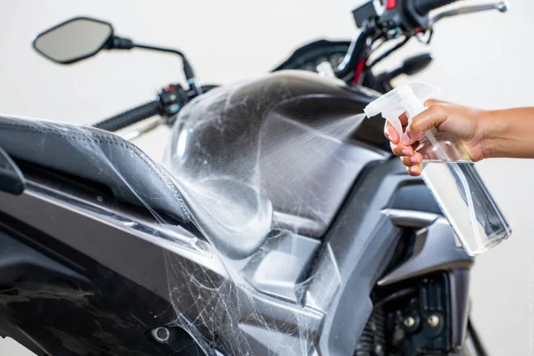 Eine Hand besprüht ein Motorrad, um Spinnennetze am Motorrad zu entfernen.